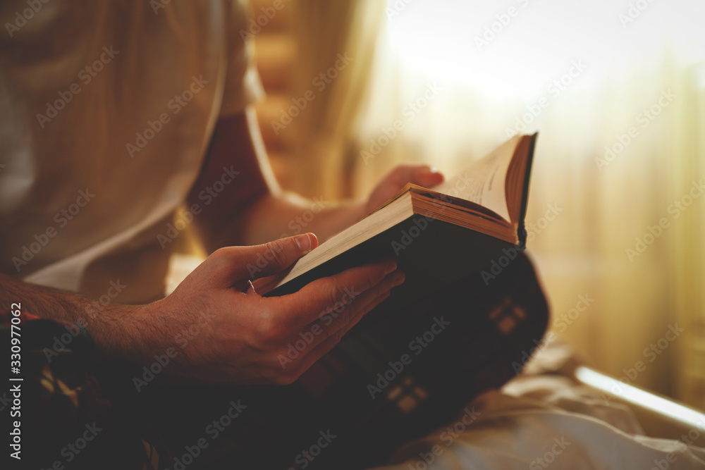 Young man reading book on bed at home, closeup - obrazy, fototapety, plakaty 