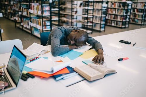 Black student sleeping in library after long preparation for exam