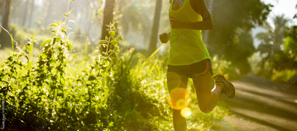 Young fitness woman running at morning tropical forest trail - obrazy, fototapety, plakaty 