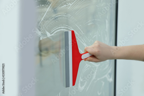 Woman cleaning window with squeegee indoors, closeup