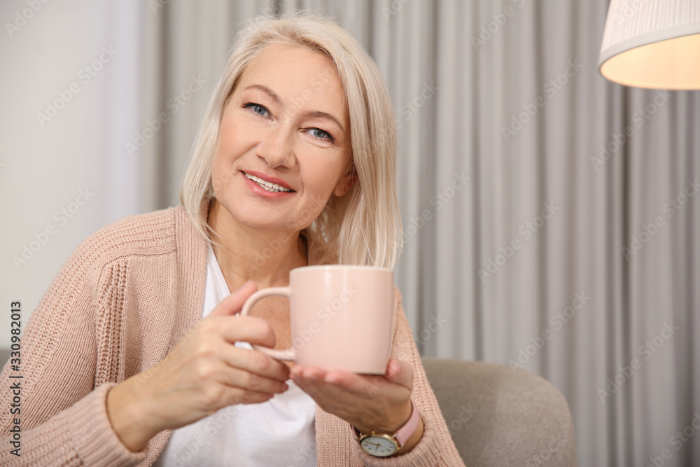 Beautiful mature woman with cup of coffee at home. Space for text