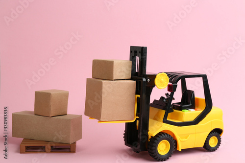 Forklift model and carton boxes on light pink background. Courier service
