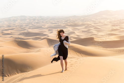 A girl in a black long dress walks through the desert. Caucasian young beautiful girl alone is in a hot, waterless desert. Runs along the sandy mountains and dunes.