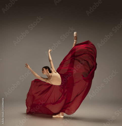 Passioned in motion. Graceful classic ballerina dancing on grey studio background. Deep red cloth. The grace, artist, movement, action and motion concept. Looks weightless, flexible. Fashion, style.