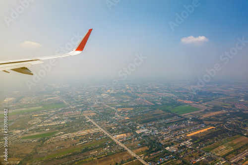 The part of airplane wing with the naturescape with sky clouds and buildings on the ground while flying. 