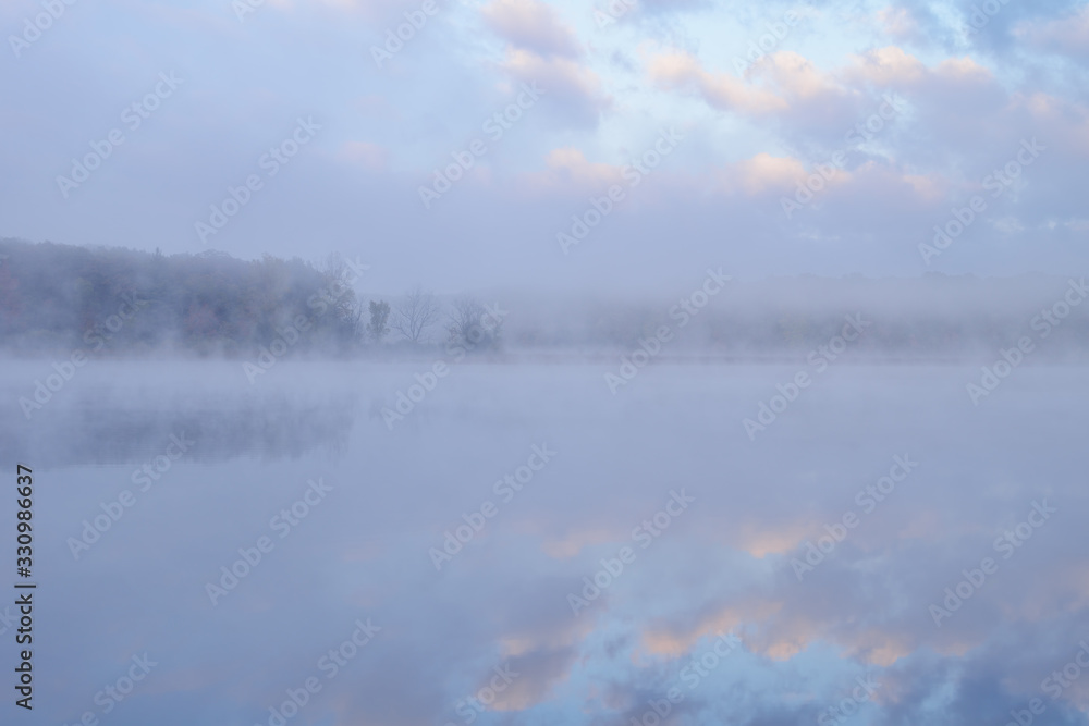 Fototapeta premium Foggy autumn landscape at twilight with reflections in calm water, Deep Lake, Yankee Springs State Park, Michigan, USA 