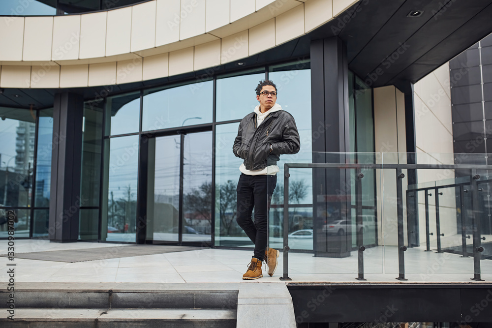 Handsome young man with curly black hair is on the street against building