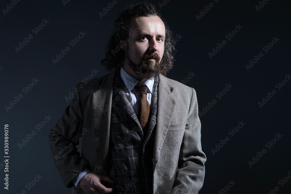 studio dramatic of a young bearded and curly-haired guy of thirty years, in an expensive business suit, holds his hand by the lapel of his jacket. On a dark background. studio dramatic of a young bearded and curly-haired guy of thirty years, in an expensive business suit, holds his hand by the lapel of his jacket. On a dark background.