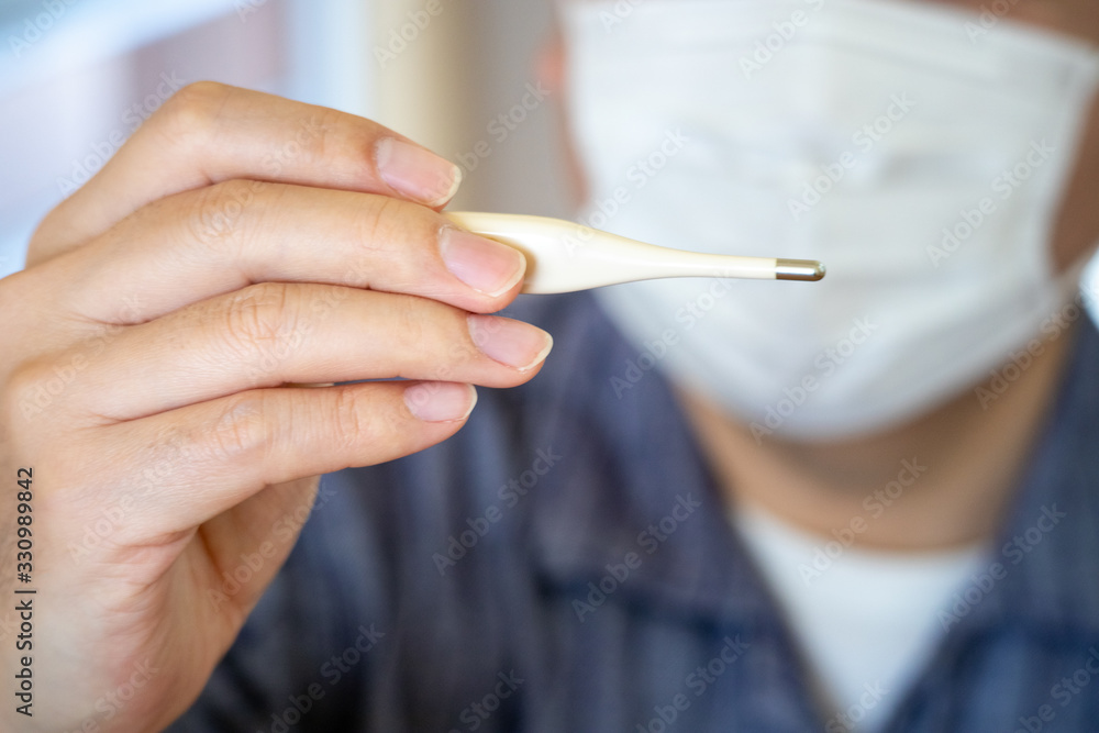 体温計で熱を測るマスク姿の男性 体温計で熱を測るマスク姿の男性