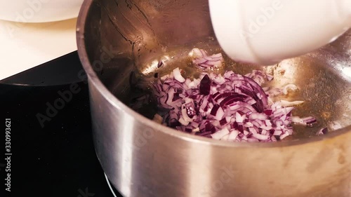 The red onion from a bowl is transferred to a large enameled pan and mixed.