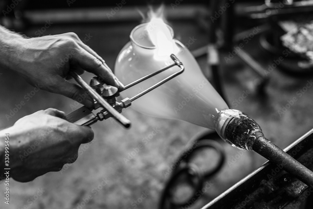 Obraz premium A close up black and white shot with shallow focus on the hand of a traditional artisan at work creating a blown glass lantern in a workshop with blowtorch.