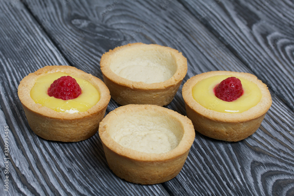 Tartlets with lemon Kurd. Decorated with raspberries. They lie on black brushed pine boards. Next to them are tartlets without toppings. Tartlets with lemon Kurd. Decorated with raspberries. They lie on black brushed pine boards. Next to them are tartlets without toppings.