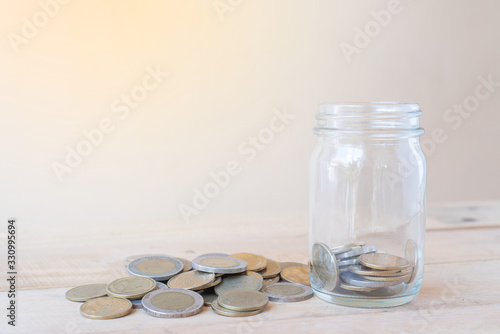 A glass bottle with a pile of coins and on wooden table - Investment, Business, Finance and Banking Concept