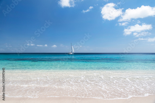 Fototapeta Naklejka Na Ścianę i Meble -  Simplistic tropical landscape with sailboat under blue skies and warm tropical water sailing across the horizon