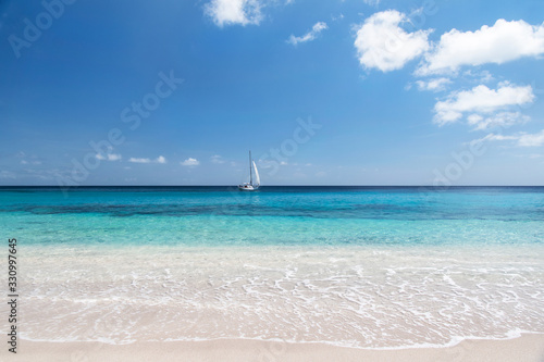 Simplistic tropical landscape with sailboat under blue skies and warm tropical water sailing across the horizon