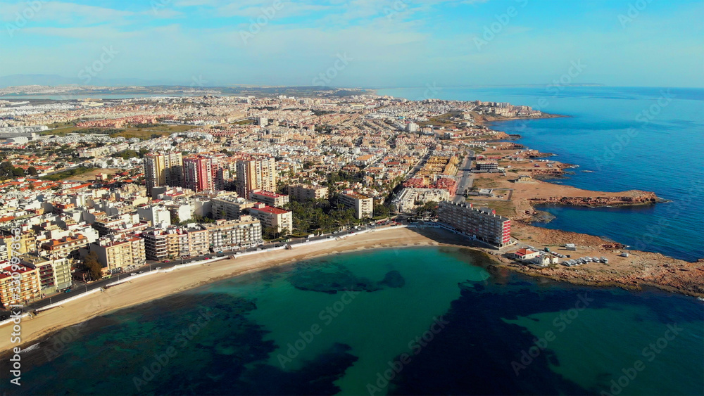 Distant aerial panoramic aerial view to Los Locos beach, white sandy coastline drone point of view, calm green turquoise color Mediterranean Sea, Torrevieja, Alicante, Costa Blanca, Spain
