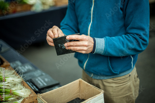 Fototapeta Naklejka Na Ścianę i Meble -  A close up shallow focus view on the hands of a market trader preparing small price tags at a stall selling organic vegetables with copy space to left.