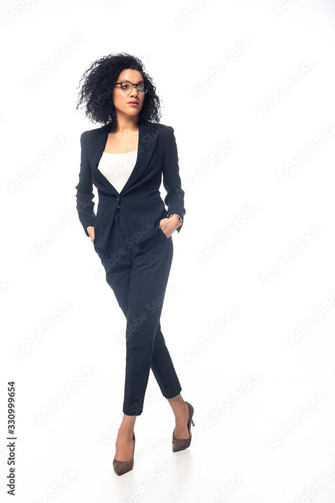 Full length view of confident african american businesswoman walking with hands in pockets on white background Full length view of confident african american businesswoman walking with hands in pockets on white background