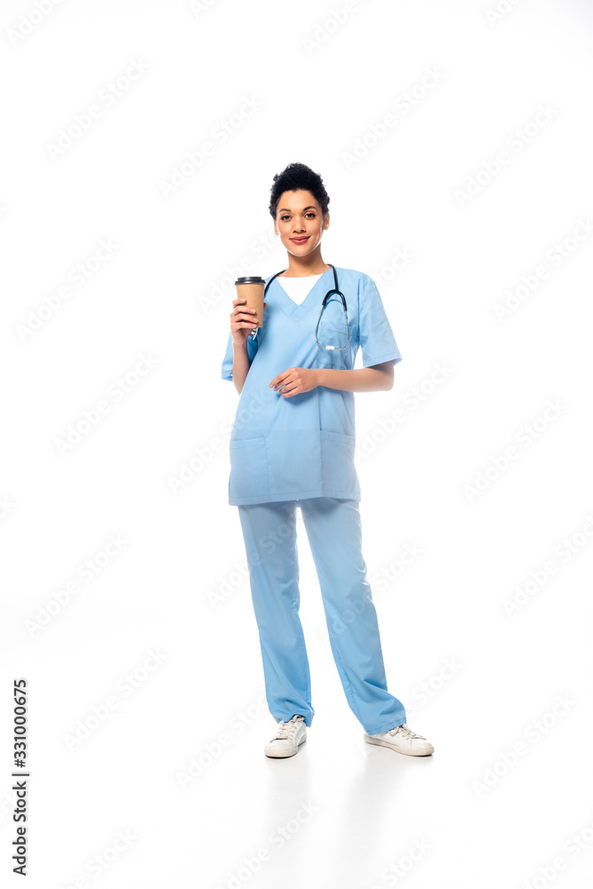 Full length view of african american nurse with stethoscope holding disposable cup of coffee on white background Full length view of african american nurse with stethoscope holding disposable cup of coffee on white background