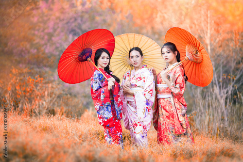 Japanese women wearing kimonos carrying red umbrellas in autumn. Beautiful Female wearing traditional japanese kimono with in autumn  Japan. Asian woman tourists.