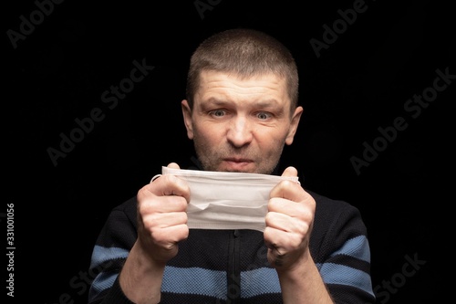 an adult man looks at a protective medical mask , and does not understand why to put it on . Protection from coronavirus infections, protection and protective measures against microbes and bacteria © Vladimir Razgulyaev