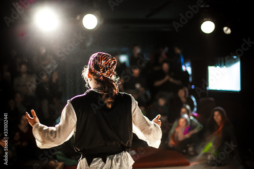 Fotografija A selective focus view from behind an actor dressed in pirate costume, performing on stage to a crowd of onlookers with blurry spot lights and copy space