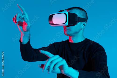 VR, AR, MR, XR-  Future technology. Neon. European man's in VR-glasses in neon on gradient background. Male portrait. Concept of human emotions, facial expression, modern gadgets and technologies