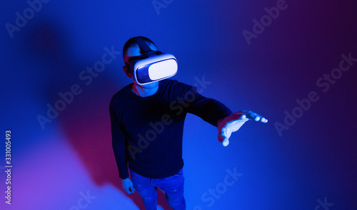 VR, AR, MR, XR-  Future technology. Neon. European man's in VR-glasses in neon on gradient background. Male portrait. Concept of human emotions, facial expression, modern gadgets and technologies