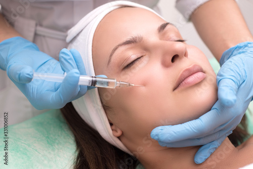 injection into the skin of the face of a young woman  close up. Doctor cosmetologist using a syringe with a needle  injects a remedy for facial wrinkles