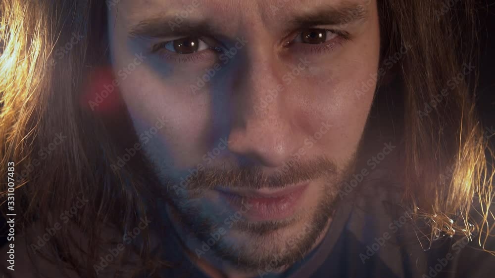 Portrait of caucasian bearded man with long hair looking at the camera, laughs nervously and sadly. Close-up. Black background. Portrait of caucasian bearded man with long hair looking at the camera, laughs nervously and sadly. Close-up. Black background.