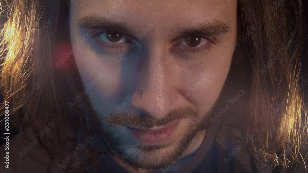 Portrait of caucasian bearded man with long hair looks at the camera with a maniac gaze and wild smile. Close-up. Black background. Portrait of caucasian bearded man with long hair looks at the camera with a maniac gaze and wild smile. Close-up. Black background.