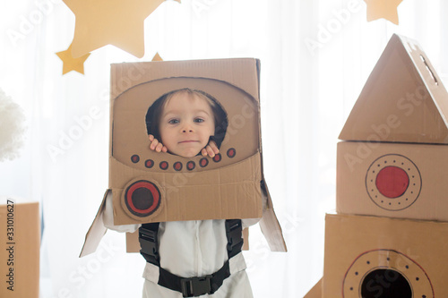 Sweet toddler boy, dressed as an astronaut, playing at home with cardboard rocket and handmade helmet photo