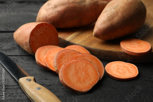 Sweet potato, board and knife on wooden background, close up