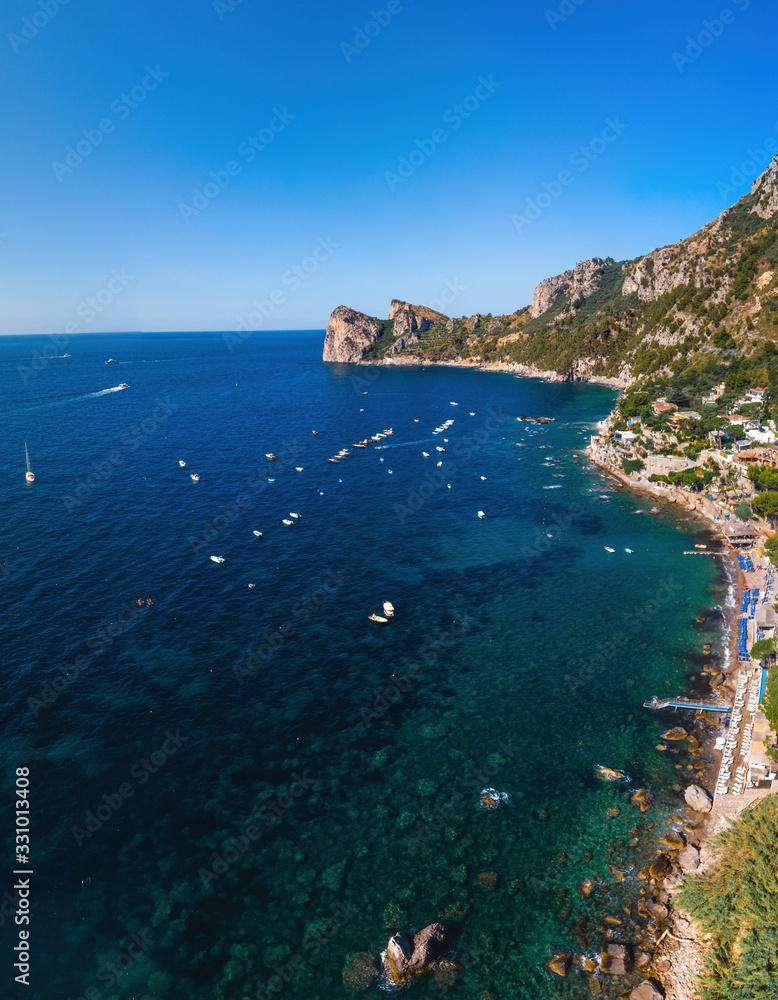Aerial view of coastline of the village of Nerano. Private and wild beaches of Italy. Turquoise, blue surface of the water. Vacation and travel concept. Boats in bay. Copy space. Vertical photo