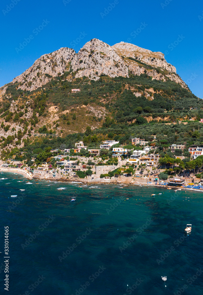Obraz premium Aerial view of coastline of the village of Nerano. Private and wild beaches of Italy. Turquoise, blue surface of the water. Vacation and travel concept. Boats in bay. Copy space. Vertical photo