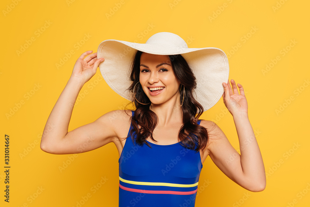 happy woman in swimsuit touching sun hat isolated on yellow happy woman in swimsuit touching sun hat isolated on yellow