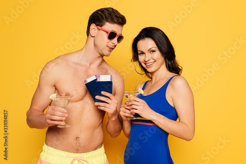 happy couple with glasses of cocktail, passports and air tickets on yellow background