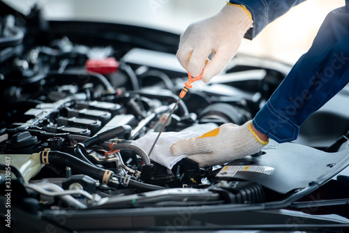 Asian car mechanic in an auto repair shop is checking the engine. For customers who use cars for repair services, the mechanic will work in the garage. photo