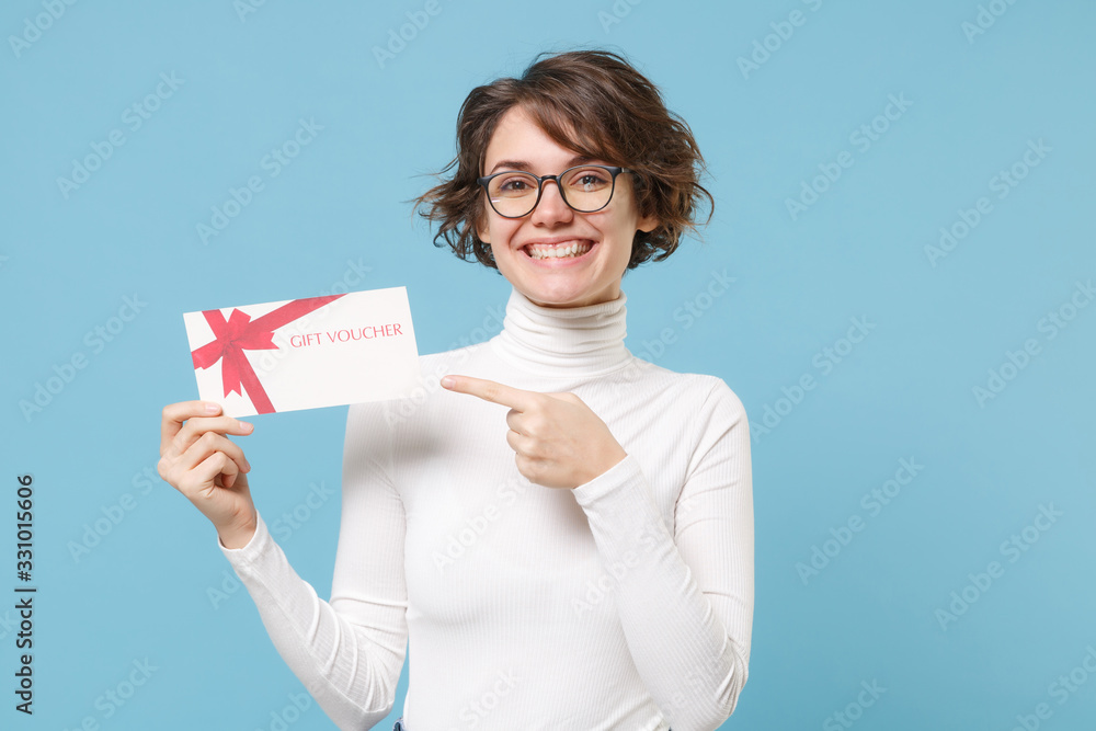 Smiling young brunette woman girl in casual white clothes eyeglasses posing isolated on pastel blue background. People lifestyle concept. Mock up copy space. Pointing index finger on gift certificate. Smiling young brunette woman girl in casual white clothes eyeglasses posing isolated on pastel blue background. People lifestyle concept. Mock up copy space. Pointing index finger on gift certificate.