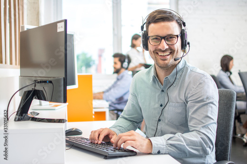 Male customer support phone operator with headset working in call centre. Group of sales agent working in office.