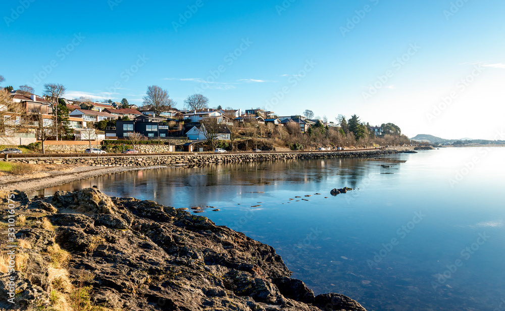 Scenic coastal view of Hafrsfjord bay covered by thin ice and residential houses of the suburb near Sword in Rock monument, Stavanger, Norway, February 2018