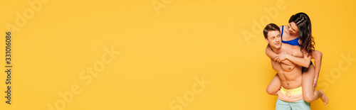 panoramic shot of handsome shirtless man piggybacking girlfriend isolated on yellow