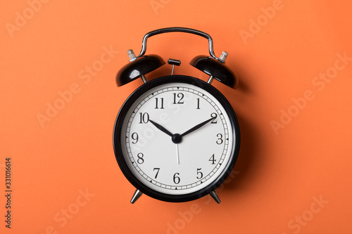 Black vintage alarm clock on orange background. Time concept