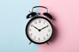 Black vintage alarm clock on blue and pink background. Time concept