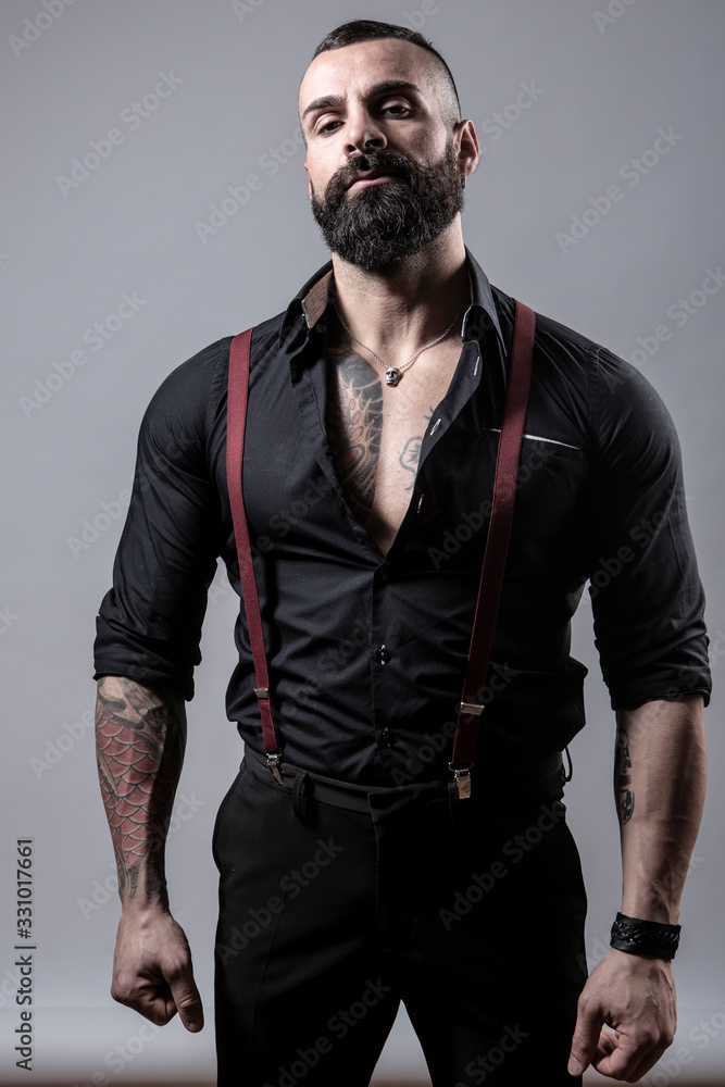 Ragazzo barbuto con Tatuaggi in tutto il corpo, vestito con camicia nera e  bretelle rosse, isolato su sfondo grigio Stock Photo | Adobe Stock