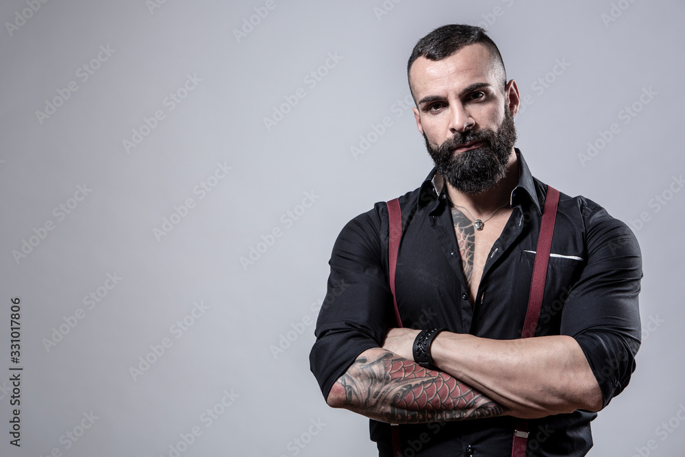 Ragazzo barbuto con Tatuaggi in tutto il corpo, vestito con camicia nera e  bretelle rosse,, incorcia le braccia, isolato su sfondo grigio Stock Photo  | Adobe Stock