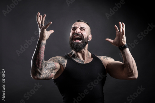 Uomo tatuato con barba urla arrabbiato , isolato su sfondo nero photo