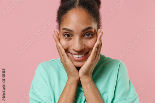 Close up of charming young african american woman girl in green sweatshirt posing isolated on pastel pink background studio portrait. People lifestyle concept. Mock up copy space. Put hands on cheeks.