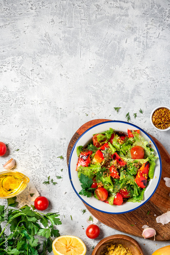 Fresh vegetable salad with dressing of mustard, olive oil, garlic, lemon and herbs in a plate on a gray concrete background, top view, copy space. Healthy mediterranean cuisine, vegetarian food