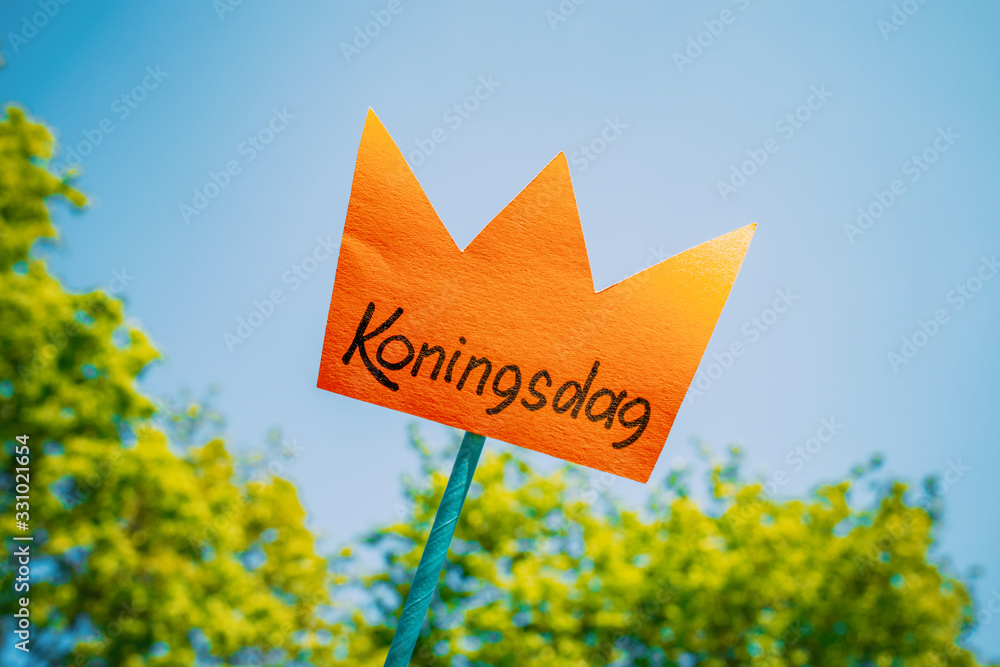 Paper cut crown with an inscription koningsdag hold with hands against blue sky